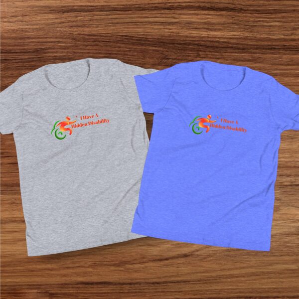 Flat lay of two youth-sized Hidden Disability Awareness t-shirts in purple and grey, displayed on a wooden surface.