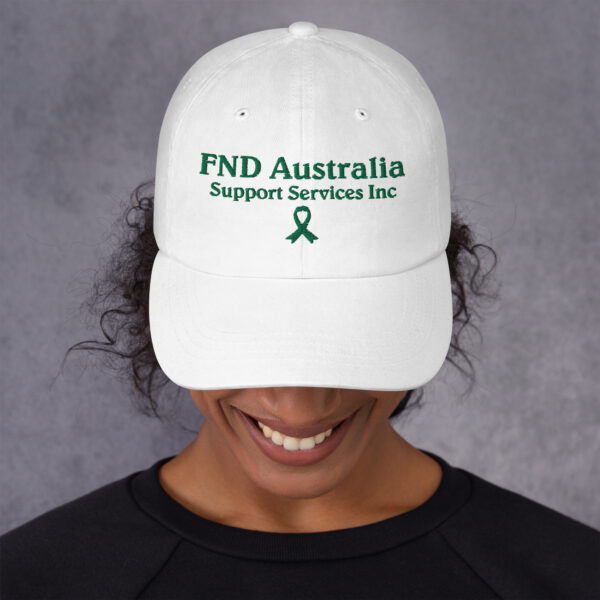 Close-up of a white low-profile FND Australia awareness hat with green embroidered ribbon and text, shown on a person from the nose down.